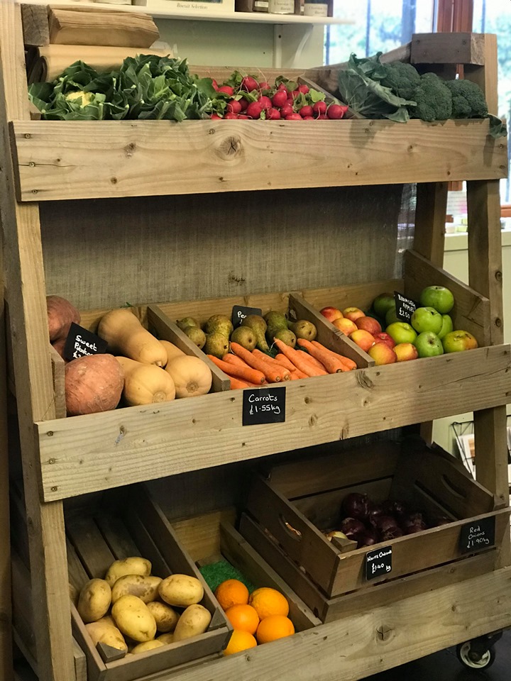A photo of a large wooden display unit containing a range of vegetables, carrots, butternut squash, broccoli, cauliflower, radishes, apples etc.