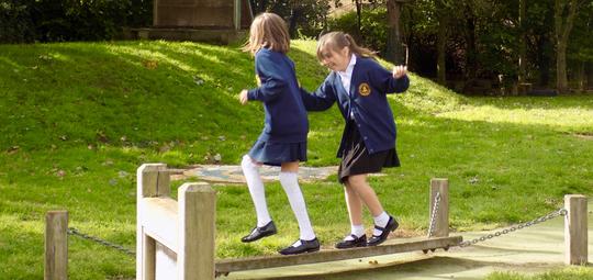 Two girls playing on a wooden beam in the grounds of Bretforton Village School