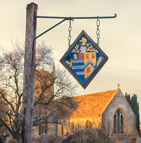 A photo of the St Leonard's Church with an old sign bearing a coat of arms in the foreground