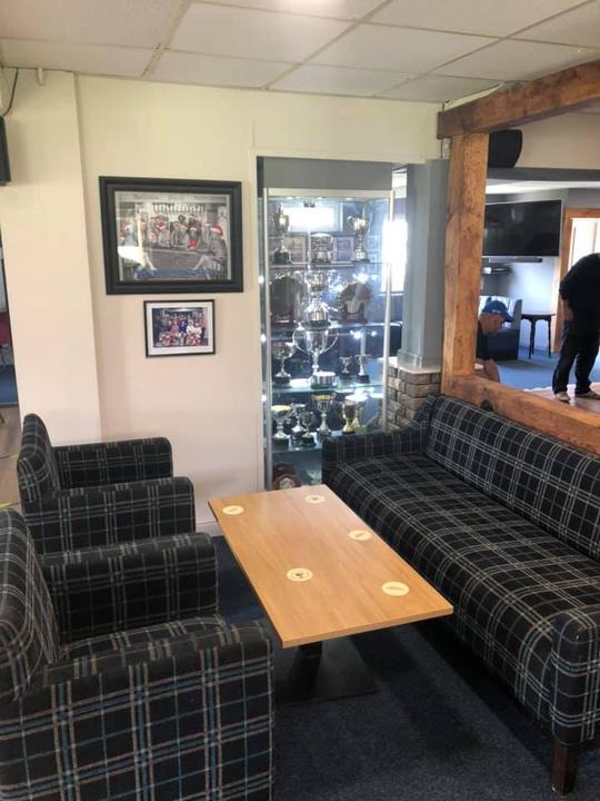 A photo of the interior of Bretforton Sports Club with a sofa, chairs and coffee table in the foreground and a trophy cabinet in the background