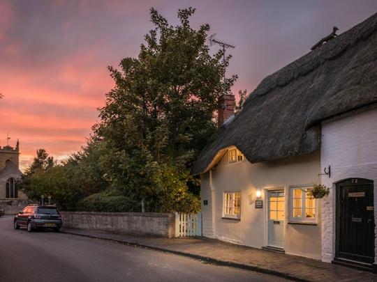 A photo of a picturesque thatched holiday cottage in Bretforton with a beautiful sunset